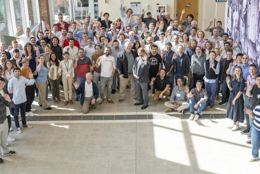 A large group of people standing in a well lit hallway in front of a mural with science images.