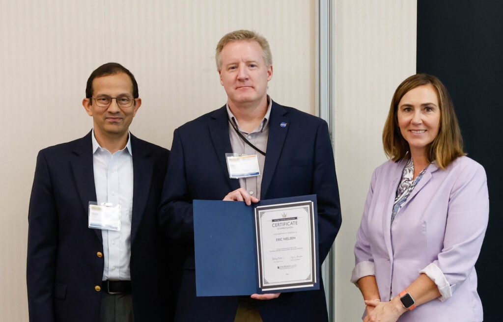 An appreciation award recipient holds a certificate while standing between two presenters during the Oak Ridge Leadership Computing Facility User Summit.