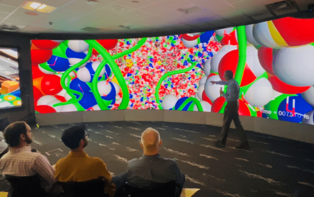 researcher points at large screen with brightly colored images of molecules