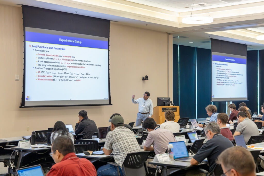 Esam El-Araby presents to attendees during the 2026 Quantum Computing User Forum at Oak Ridge National Laboratory, using presentation slides and demonstrating a prototype circuit board while discussing quantum computing research.