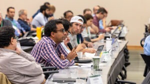 Herschel Chawdhry speaks into a handheld microphone while asking a question during the discussion session at the Quantum Computing User Forum (QCUF) 2026 as fellow attendees listen.